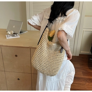 Détail d'un sac cabas en paille tressée beige avec anses en cuir dans un décor chaleureux