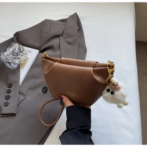 Detail of a brown pleated crossbody bag featuring fashion text and a white plush pendant charm