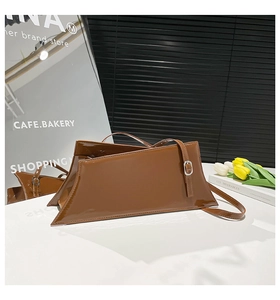 Detail of a brown glossy patent leather asymmetric shoulder bag with silver hardware buckle