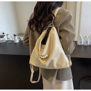 Détail du sac triangle crème avec de grandes perles et des accents de chaîne dorée