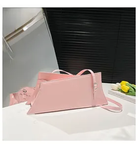 Detail of a pink asymmetric geometric tote bag featuring a glossy patent finish and slim strap
