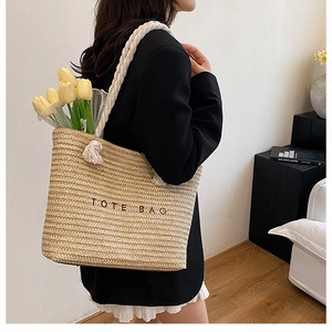 Detailed texture of woven straw tote bag with black embroidered lettering and cotton rope straps