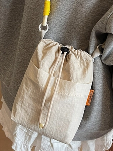 Beige mesh drawstring crossbody bag with orange logo tag and yellow woven shoulder strap