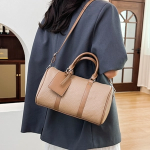 Detail showing woman wearing a camel lychee grain barrel bag with twin handles and strap