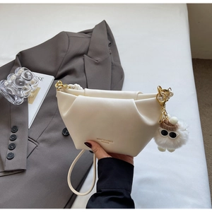 Detail of white pleated cloud bag featuring golden hardware and plush monster charm
