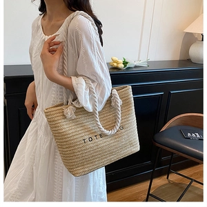 Detailed view of beige straw tote bag with white cotton rope handles and TOTE BAG text