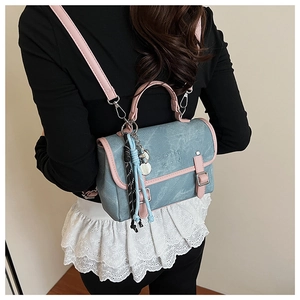Detail of light blue denim backpack with pink leather trim and trendy charms