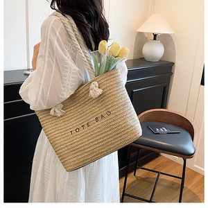 Detail of hand-woven straw tote bag with cotton rope handles and embroidered text