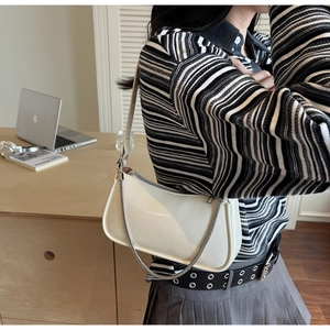 Modèle portant un sac hobo en cuir verni crème avec chaîne argentée et longue bandoulière