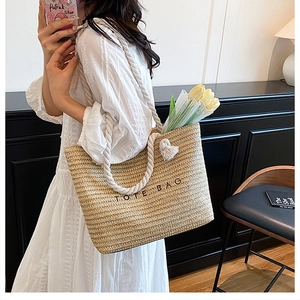 Straw tote bag detail featuring white cotton rope handles and embroidered text decoration