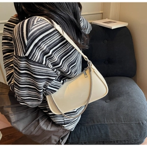 Détail d'un sac sous le bras en cuir blanc crème avec chaîne en argent sur un canapé gris