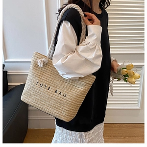 Detail of woven straw tote bag with black TOTE BAG text and thick white cotton rope handles