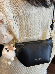 Minimalist black crossbody bag with geometric pleats and white plush charm on a model