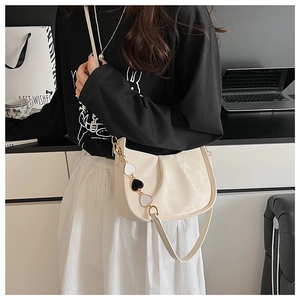 Vue détaillée du sac plissé crème avec chaîne dorée et pendentif en forme de cœur