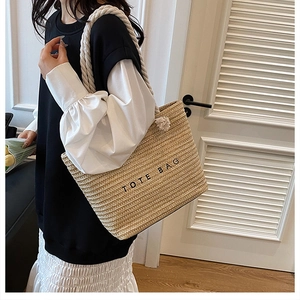 Detail of woven straw tote bag featuring rope handles and black printed lettering