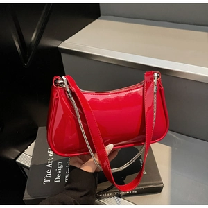 Gros plan du sac baguette en cuir verni rouge avec chaîne argentée sur livres