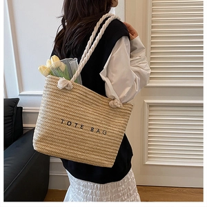 Detail view of woven straw tote bag with white rope handles and tulip decoration