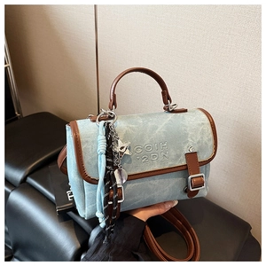 Detail of light blue denim tote bag with brown leather handles and star charm