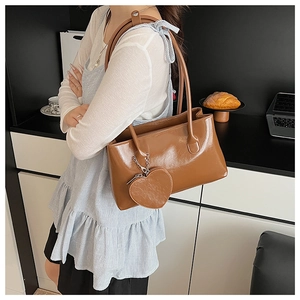 Caramel brown leather shoulder bag with a stylish heart-shaped charm shown on a model