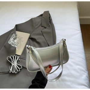 Détails du sac baguette argenté avec chaîne sur literie blanche et costume gris chic