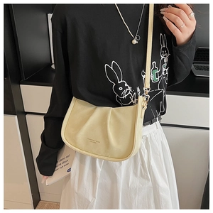 Détail du sac demi-lune crème avec design plissé et bandoulière porté par un mannequin