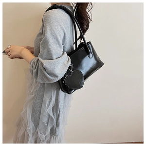 Detail view of black glossy leather underarm bag with a silver heart-shaped coin purse charm