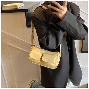 Detail of light yellow underarm bag showing faux leather texture and utility flap pockets