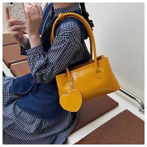 Detail of bright yellow faux leather tote bag featuring a cute heart-shaped charm accessory