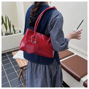 Detail of red patent leather shoulder bag with heart pendant worn on a denim outfit