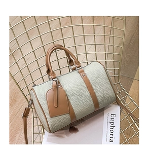 Detailed view of green Boston bag with brown leather handles on a gold chair with magazine
