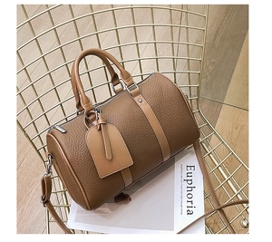 Brown litchi grain Boston bag with dual handles and strap displayed on a magazine