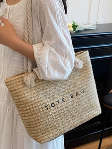 Summer straw tote bag with black TOTE BAG text and tassel detail for beach vacation