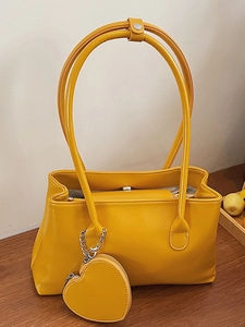 Minimalist ginger yellow tote bag with long shoulder strap and heart-shaped pendant detail