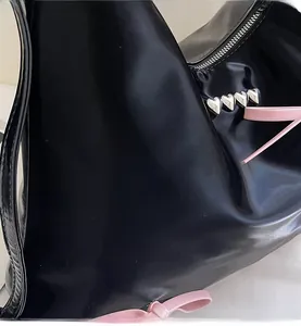 Close-up of black glossy tote bag featuring pink leather bow and silver heart rivets