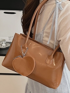 Brown glossy patent leather shoulder bag with heart pendant shown on model
