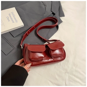 Detail of dark red high-gloss shoulder bag with double pockets on a grey suit