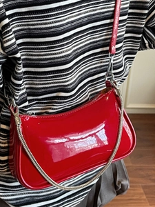 Sac demi-lune en cuir verni rouge brillant avec chaîne argentée porté par un mannequin