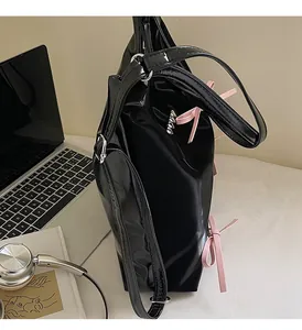 Detail showing glossy black patent leather shoulder bag with pink decorative bows