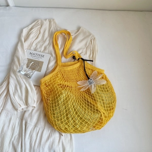 Detail einer gelben Netztasche mit weißem Blumenanhänger auf einem weißen Sommerkleid