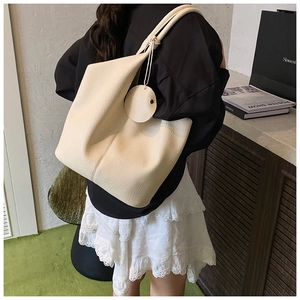 Woman carrying large cream lychee leather tote bag with slim straps in a minimalist indoor setting