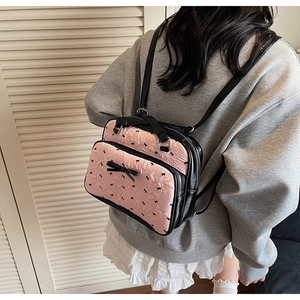 Rear view of a pink bow-print backpack worn by a model in a minimalist home setting