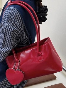 Glossy red faux leather tote bag with heart charm shown on model in a chic studio setting