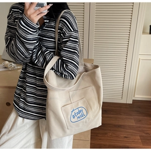Detail view of cream canvas tote bag featuring blue logo embroidery and front pocket