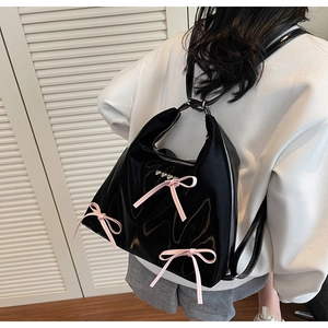 Detail view of black glossy backpack with pink bows and heart buckles on a female model