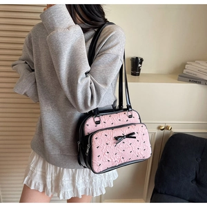 Detailed close-up of pink shoulder bag with black bow prints and smooth leather straps
