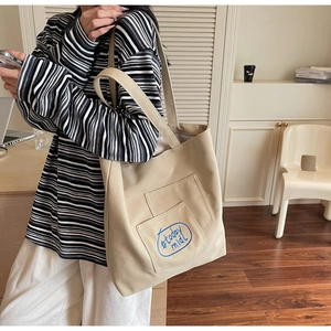 Detail of beige canvas tote with blue embroidery and side pocket in a lifestyle setting