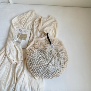 Detail der cremefarbenen Netztasche mit Blumenanhänger und gewebter Hohlstruktur