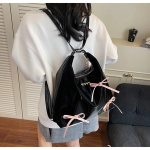 Detail view of glossy black faux leather backpack with pink ribbon bows and heart zipper