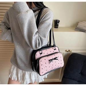Pink shoulder bag detail showing relief bow patterns and glossy black leather strap texture
