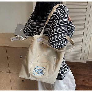 Detail shot of beige canvas tote bag with embroidered blue pattern and sturdy double straps